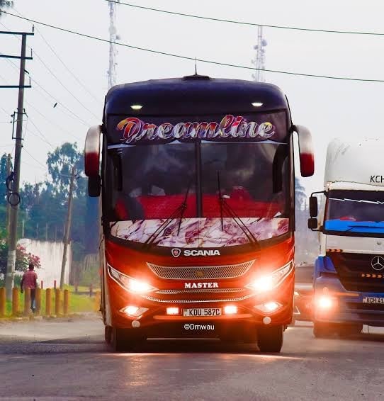 Front view of a Scania Dreamline coach bus with illuminated headlights and red and blue livery on a highway